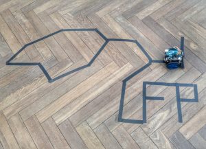 Line-following robot on a track taped to a wooden floor, spelling UFP