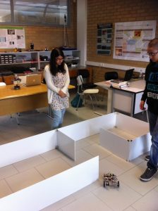 Labirinto para robôs construído com paredes brancas no chão, com alunos ao lado