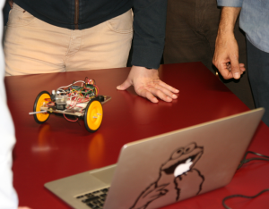 Small wheeled robot on a red table next to a laptop